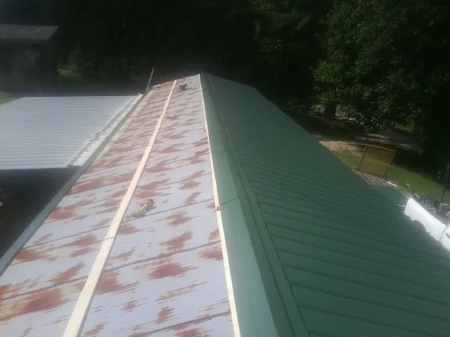Old rusted panels beside newly installed green metal roofing — Wind Damage Roof Repair by Roofing Brothers in Locust Grove