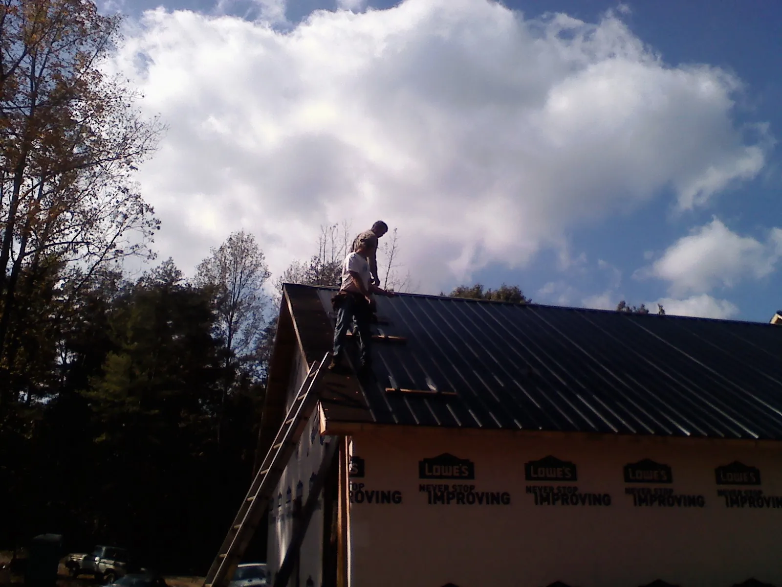 Roofer fastening dark metal panels high against a cloudy sky, from a Roof Inspection job in Locust Grove